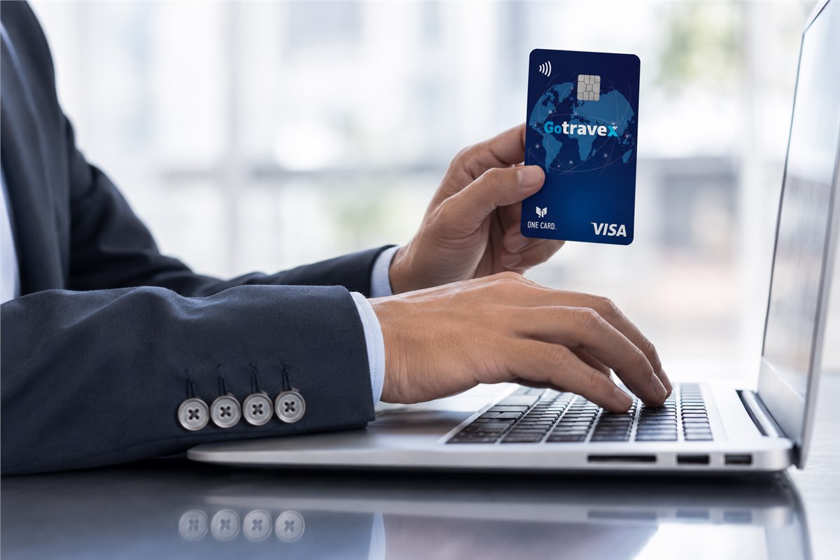 Ejecutivo usando una computadora y mostrando la tarjeta GoTravex Visa